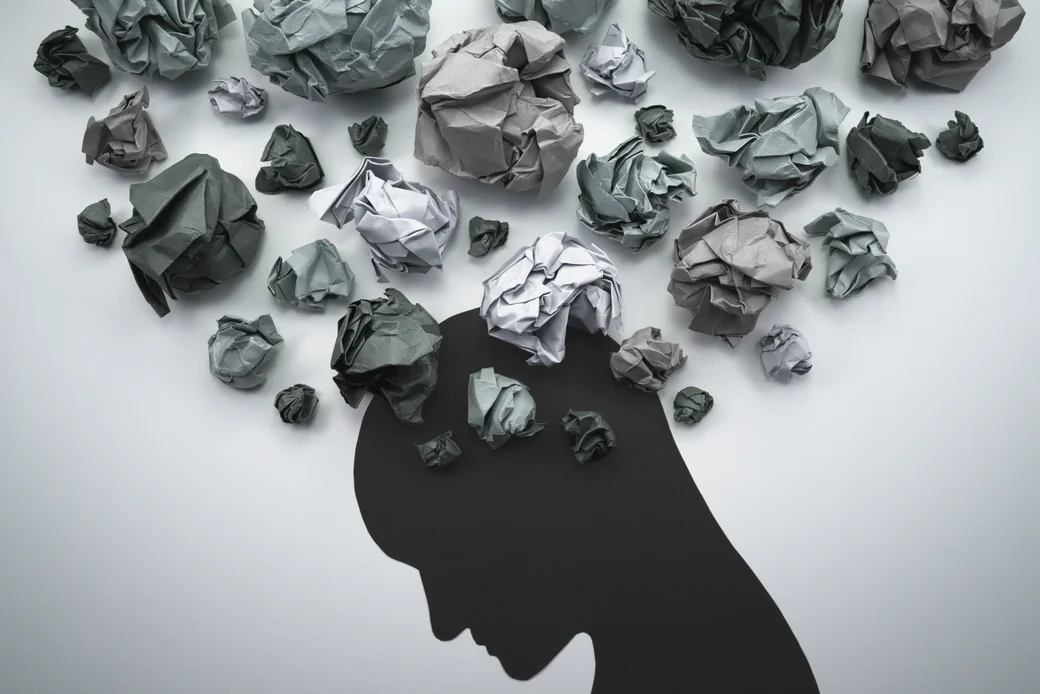 Silhouette eines Kopfes mit grauen Papierknäueln als Symbole für belastende Gedanken